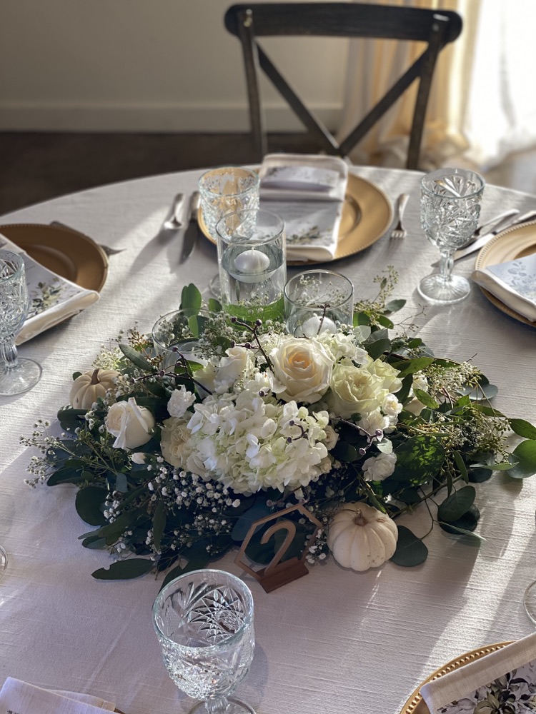 White roses and hydrangea centerpiece with small pumpkins on a set table