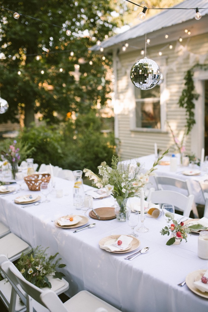 Long table set under string lights and a disco ball, wildflower centrepieces in the evening sun