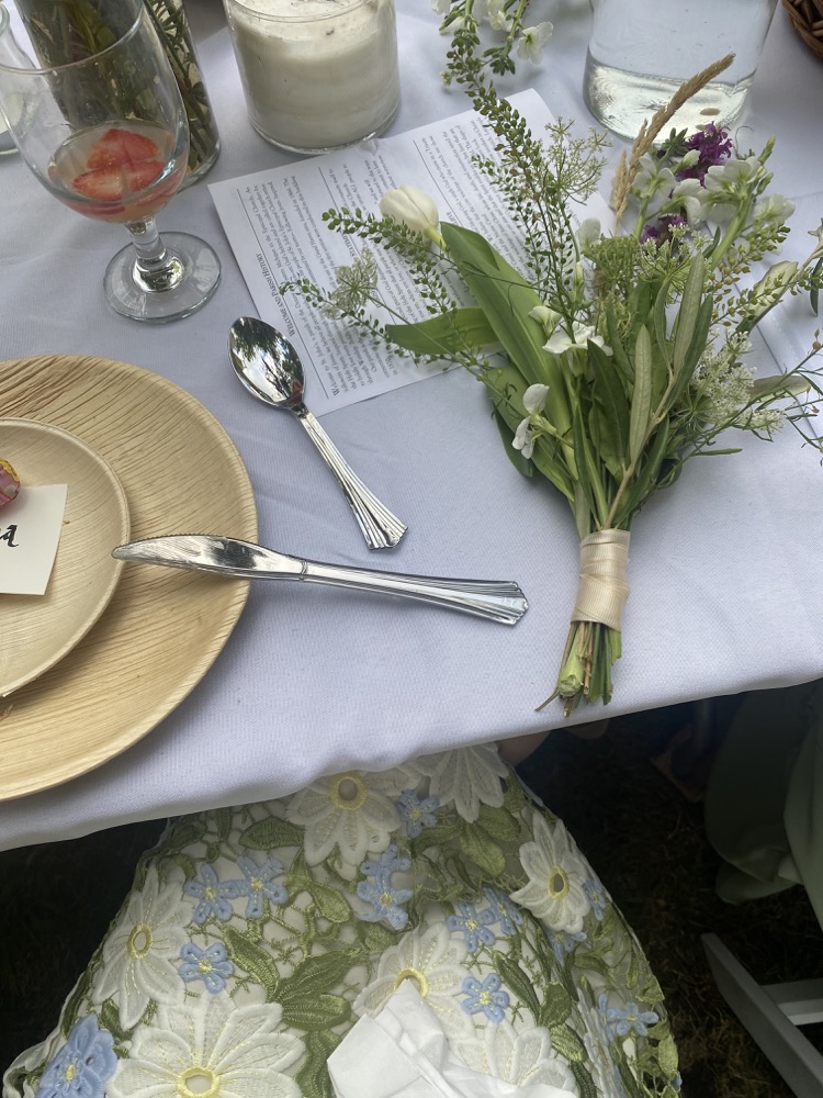 Wildflower bouquet tied with ribbon resting beside a wedding program and place setting
