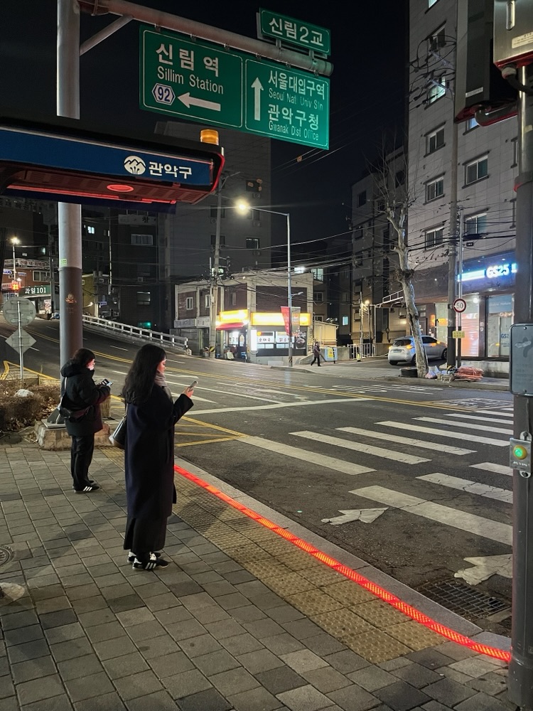 A red LED strip glowing along the edge of a Seoul crosswalk at night