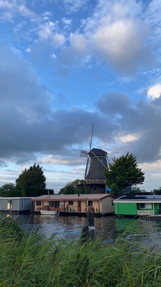 A windmill rising behind houseboats on the water, Badhoevedorp
