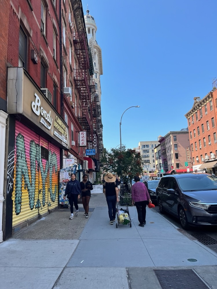 A woman wheeling an oxygen supply along a Chinatown sidewalk, New York